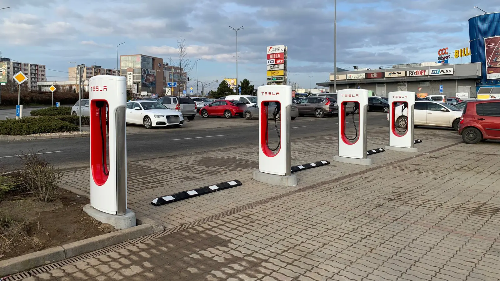 Four red and white Tesla Supercharger stalls in a shopping-center parking lot in Košice, Slovakia