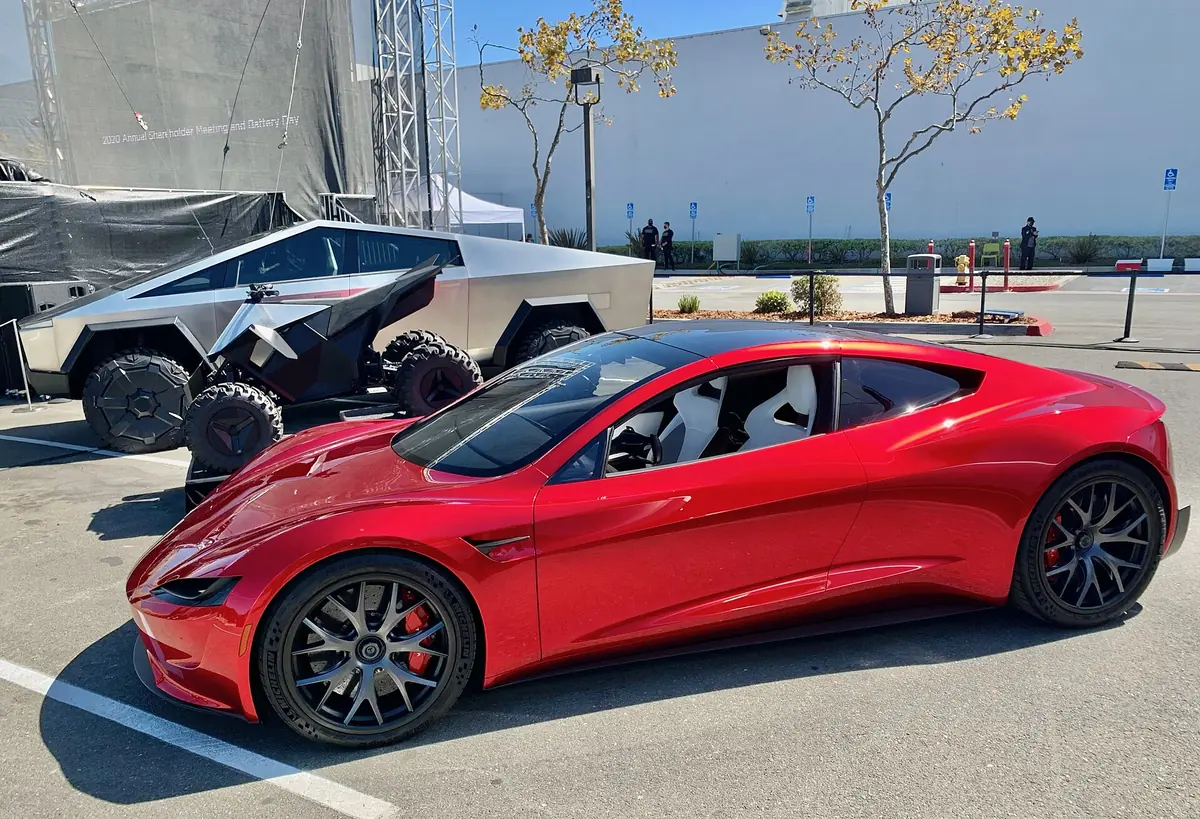 Red second-generation Tesla Roadster prototype parked outdoors beside a Cybertruck and Cyberquad at the 2020 Tesla Annual Shareholder Meeting and Battery Day