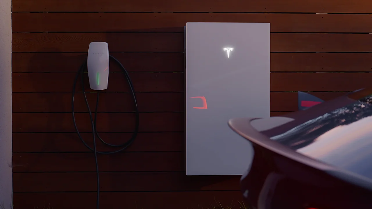 Tesla Wall Connector and Powerwall 3 mounted on a wood-slat wall beside the rear of a red Tesla